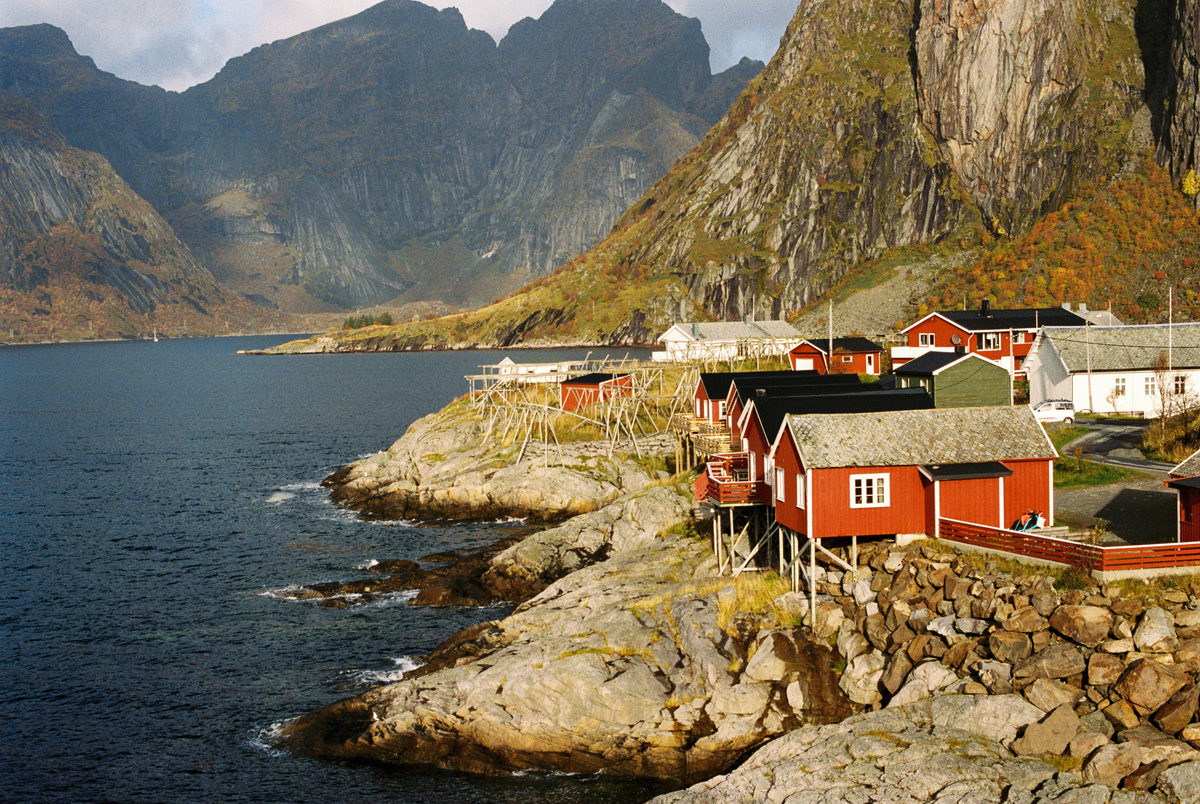 Red fishermen’s cabins on rocks below towering mountains