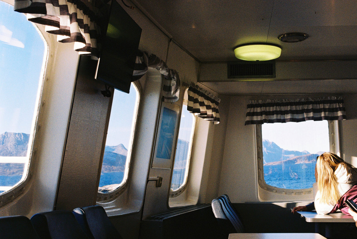 A woman by the window of a ferry, sea and mountains beyond