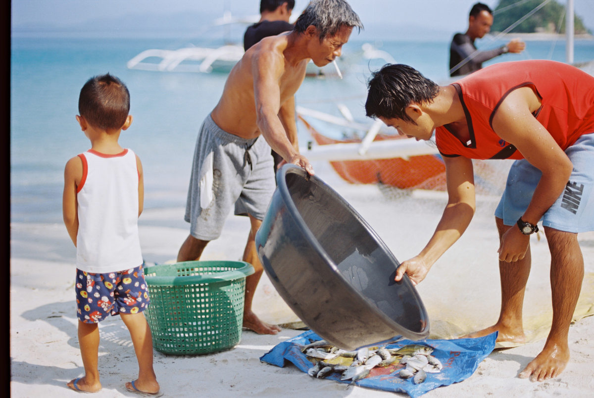 Fishermen and a child sorting the catch on the beach