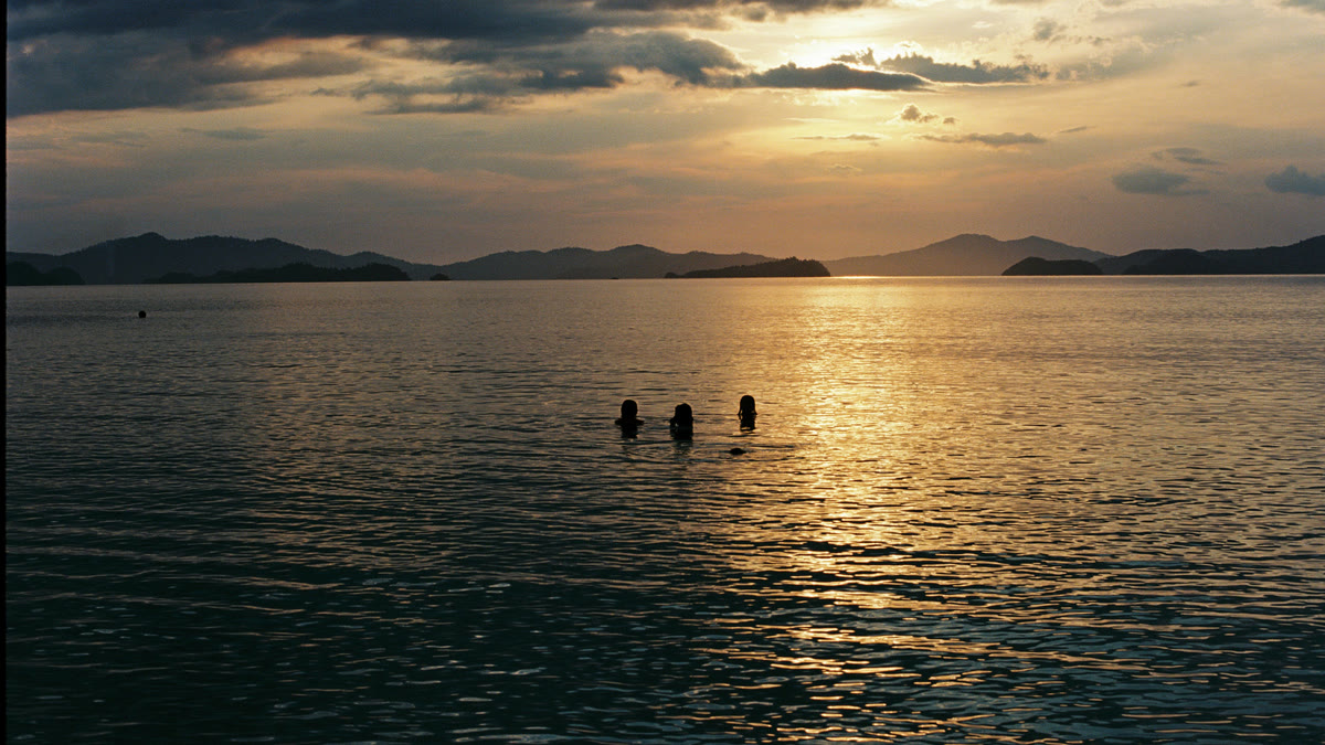 Sun setting over the water, swimmers in the glittering light