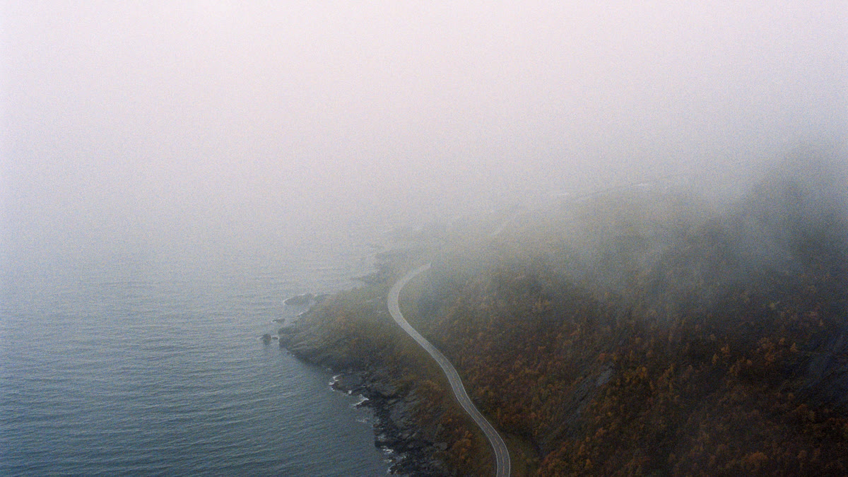 Mist rolling over a coastal road and dark water
